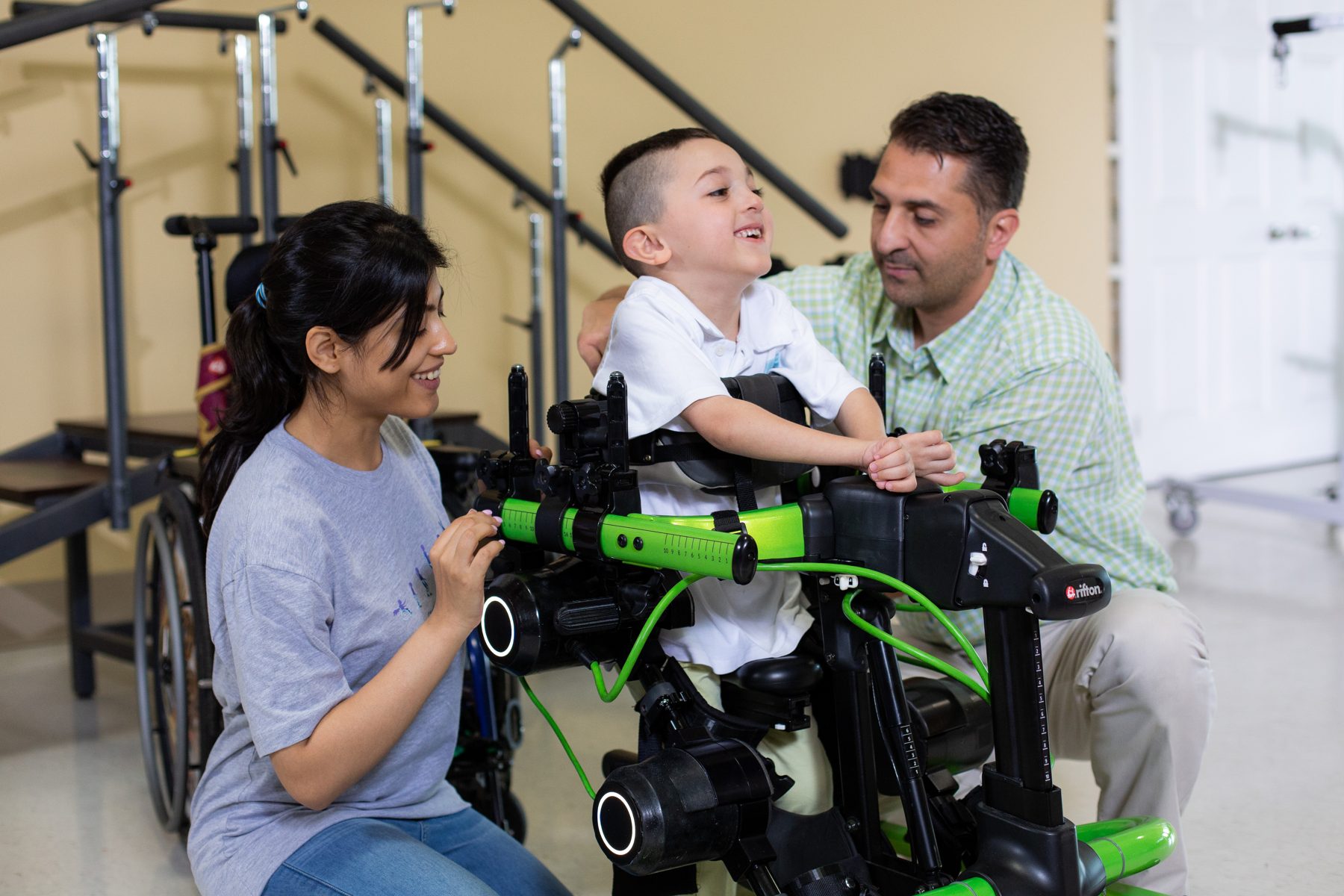 A physical therapist and a parent with a child standing in a Trexo at a clinic